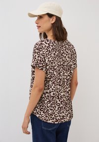 T-shirt à manches courtes en beige avec un imprimé léopard brun, présentant un dos plissé et des manches retroussées, associé à un jean bleu foncé.