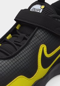 Κοντινό πλάνο μαύρου και κίτρινου αθλητικού παπουτσιού με επάνω μέρος από δίχτυ, ελαστικά κορδόνια, ιμάντα βέλκρο και λογότυπο «air» στη γλώσσα.