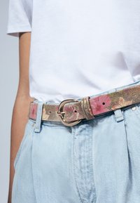 Ceinture à motif floral en doré métallisé, avec des accents roses et oranges. Comprend une boucle arrondie en ton argenté et des trous ajustables.