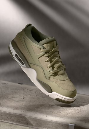Zapatillas de deporte verde olivo con una parte superior texturizada, superposiciones suaves y acentos blancos. Cuenta con cordones, una suela de goma y amortiguación de aire visible.
