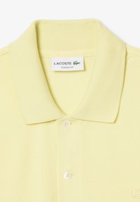 Gul polo-shirt med ribbet krave, to-knap lukning og et lille broderet logo på venstre bryst. Klassisk pasform og tekstureret stof.