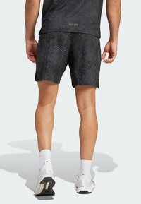 Crne sportske šorceve s teksturiranim dizajnom, nošene s bijelim čarapama i svijetlosivim tenisicama. Pojas sadrži oznaku logotipa.