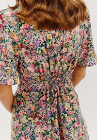 Květinové šaty s krátkými rukávy, se smockovaným pasem. Tkanina zobrazuje pestrou paletu květin na zeleném pozadí.