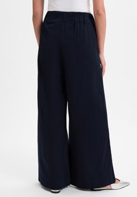 Marineblauwe wijde broek met een elastische tailleband, gemaakt van lichte stof, met een gladde textuur en een getailleerde pasvorm aan de zoom.