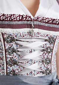 Gorsetowy fason góry z białą satynową wstążką, srebrnymi dekoracyjnymi haczykami, skomplikowanym materiałem w czerwone i niebieskie kwiaty oraz falbaniastym wykończeniem.