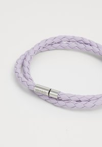 Pulsera trenzada de cuero morado claro con un cierre de metal tono plata, con el logotipo "HUGO" en relieve. Textura suave y diseño flexible.