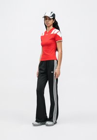 Top deportivo rojo de manga corta con detalles blancos, combinado con pantalones negros con franjas blancas laterales y zapatillas deportivas grises.