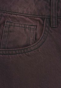 Zbliżenie na ciemnobrązowy denim, pokazujący przednią kieszeń i pętlę na pasek z widocznym przeszyciem i fakturą.