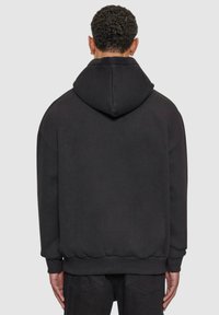 Pulletrøye med hette i svart, med stor hette, ribbestrikkede mansjetter og nederkant. Glatt tekstur med minimalistisk design.