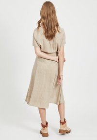 Robe beige à pois avec des manches courtes, une jupe fluide et une taille cintrée, associée à des bottines beige et rouge.