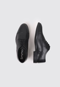 Zapatos de cuero negro con un acabado suave, diseño de cordones y sutiles detalles perforados en los laterales. Suelas planas.