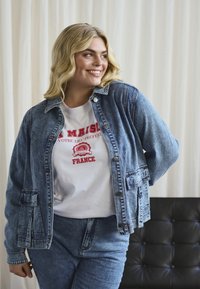 Nattblå denimjacka med avslappnad passform, med två framfickor och tryckknappar. Vit t-shirt under med röd grafisk tryck.