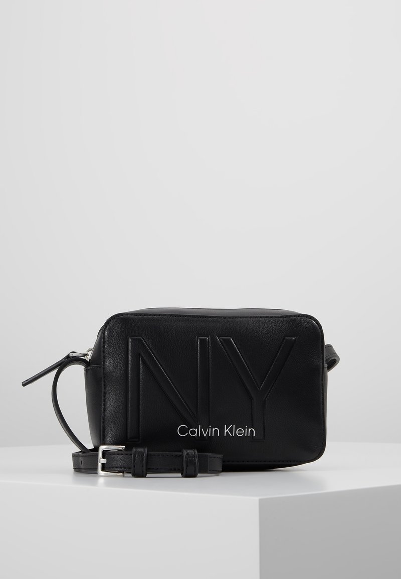 Borsa in pelle nera con design in rilievo "NY" e testo "Calvin Klein". Forma rettangolare, tracolla regolabile e chiusura con zip. Tessuto liscio.