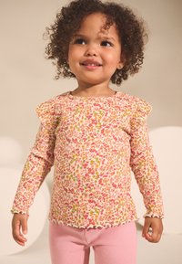 Pikad varrukad kollase-rohelise-roosa lillemustriga top, millel on volangidega õlad ja laineline ääris. Sobitatud roosade soonikuga retuusidega.