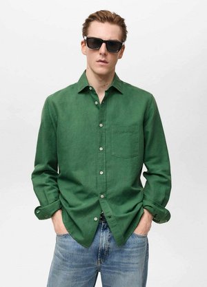 Green long-sleeve linen shirt with a button-down collar, front pocket, and white buttons, paired with blue denim jeans.