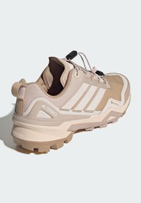 Beżowe buty trekkingowe z siateczki i syntetycznych materiałów, charakteryzujące się teksturowaną cholewką, kontrastującymi białymi paskami oraz ruggedową podeszwą.