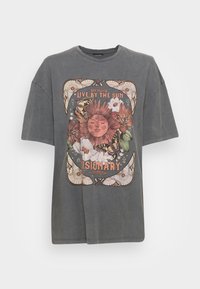 Camiseta gris de talla grande con un gráfico central de un sol con elementos florales, mariposas y el texto "Live By The Sun Visionary".