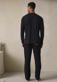 Zwarte top met lange mouwen en bijpassende broek van zachte stof, met een slanke pasvorm en minimalistisch ontwerp, gezien vanaf de achterkant.