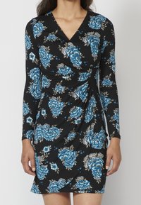Schwarzes Kleid mit langen Ärmeln und tiefem V-Ausschnitt, verziert mit blauen und weißen Blumenmustern, mit seitlichen Raffungselementen.