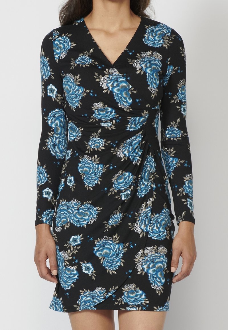 Schwarzes Kleid mit langen Ärmeln und tiefem V-Ausschnitt, verziert mit blauen und weißen Blumenmustern, mit seitlichen Raffungselementen.