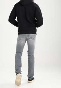 Sudadera negra con capucha, combinada con jeans gris claro. Las zapatillas tienen un upper negro y suela beige. Diseño simple con mínimos detalles.