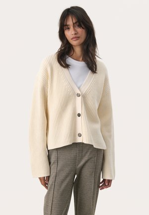 Roomkleurige ribgebreide cardigan met een V-hals, vijf knopen en een verlaagde schouderlijn. Draag het over een witte blouse, gecombineerd met geruite broeken.