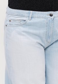 Lyseblå denimjeans med en jevn tekstur, som har to sidelommer, kontraststing og en enkelt svart knapp i midjen.