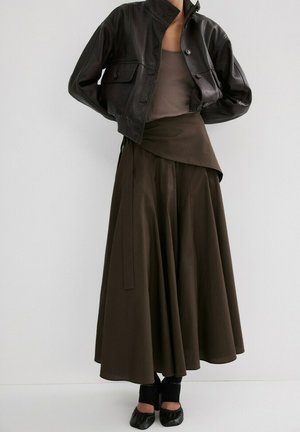 Femme portant une veste en cuir noire coupée, un haut marron sans manches, une jupe large taille haute marron foncé, et des ballerines noires.