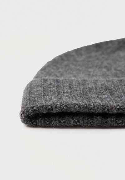 Chapéu de lã cinzento escuro dobrado com textura canelada, visto de lado em close-up, sobre uma superfície branca.