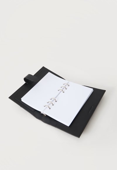 Classeur en cuir noir ouvert avec des feuilles blanches vierges à anneaux métalliques sur fond blanc.