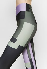 Legginsy z wysokim stanem z geometrycznym wzorem w kolorach zielonym, czarnym i lawendowym. Wykonane z gładkiego, elastycznego materiału o eleganckim kroju.