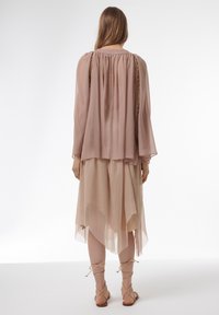 Blusa transparente de color rosa claro con cuello fruncido y mangas largas, combinada con una falda asimétrica de color beige y sandalias con tiras.