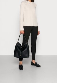 Kremowy prążkowany sweter z szerokim kołnierzem, czarne legginsy oraz duża czarna skórzana torba na ramię z chwostem i złotymi detalami.