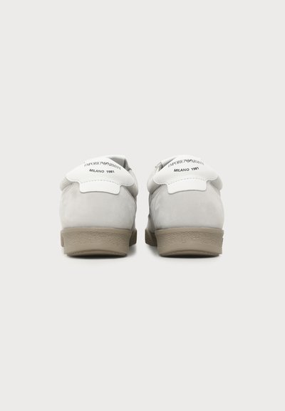 Paire de baskets gris clair avec semelles beige vues de dos, dotées d'onglets de talon blancs étiquetés "EMPORIO ARMANI MILANO 1981."