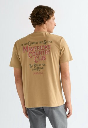 Taupekleurig katoenen T-shirt met een afbeelding in rood en zwarte tekst op de achterkant, met de tekst "Mavericks Country Club" en gerelateerde zinnen, voorzien van korte mouwen.