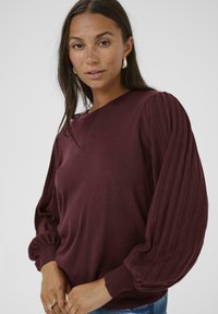 Pull en tricot bourgogne avec des manches ballon côtelées et des poignets ajustés ; texture douce et col rond.