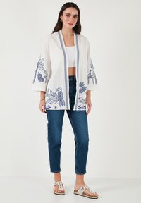 Valge kimono jakk siniste lillede tikandiga, avatud ees, 3/4 varrukatega. Koos kõrge vöökohtadega siniste teksade ja mustriliste sandaalidega.