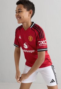 Röd Manchester United-tröja med svarta detaljer och r�änder. Har vita sponsorlogotyper och "DXC Technology" på ärmen. Kombineras med vita shorts.