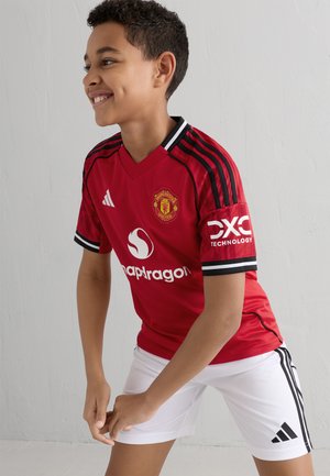 Red Manchester United jersey with black accents and stripes. Features white sponsor logos and "DXC Technology" on the sleeve. Paired with white shorts.