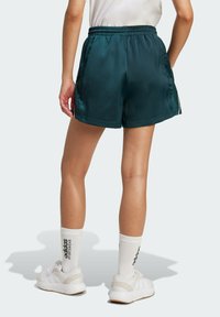 Satinové tyrkysové šortky s elastickým pasem, bočními kapsami a kontrastními bílými detaily, doplněné bílými teniskami a ponožkami do délky crew.