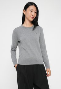 Szary sweter dzianinowy z długimi rękawami i okrągłym dekoltem. Posiada małe logo na piersi oraz ściągacze przy rękawach i na dole. Dopasowany krój.