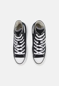 Black canvas high-top sneakers with white rubber toes, thick white laces, and contrasting stitching detail. Rounded shape and textured surface.
