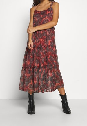 Vestido maxi en rojo y negro con patrón de hojas, volantes en capas, tirantes finos y un tejido ligero y fluido. Combinado con botas de vaquero negras.