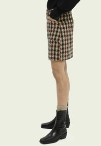 Tjekket mini-skort i brun, sort og creme; med sidelommer og snor i taljen. Båret med sorte ankelstøvler og strikkede sokker.