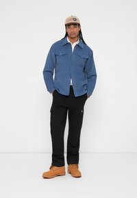 Denim skjorte med knaplukning og brystlomme, sorte cargobukser og tan lace-up støvler. Lyseblå farve, medium vægt stof, afslappet design.