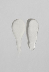 Deux gouttes de liquide texturé sur un fond gris clair ; l'une blanche, lisse et nacrée, l'autre claire avec une finition brillante.