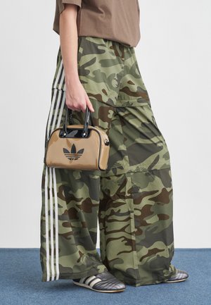 Pantalons cargo larges en camouflage avec des rayures blanches, associés à un petit sac à main beige avec un logo noir, et des chaussures de sport grises.