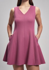Robe courte sans manches de couleur rose, avec un décolleté en V, jupe évasée, tissu texturé et poches de chaque côté. Design simple et décontracté.