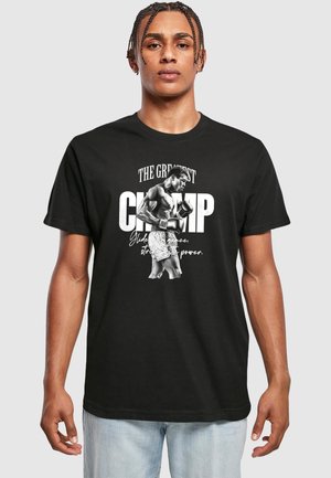 Sort bomulds t-shirt med et stort grafik af en bokser og teksten: "The Greatest CHAMP" i hvid med kursiv accentuerede elementer. Klassisk crew neck-design.