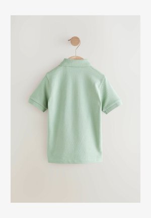 Fakó zöld, rövid ujjú pólóing rücskös gallérral és textúrált anyaggal, egy fa akasztón bemutatva, világos háttér előtt.